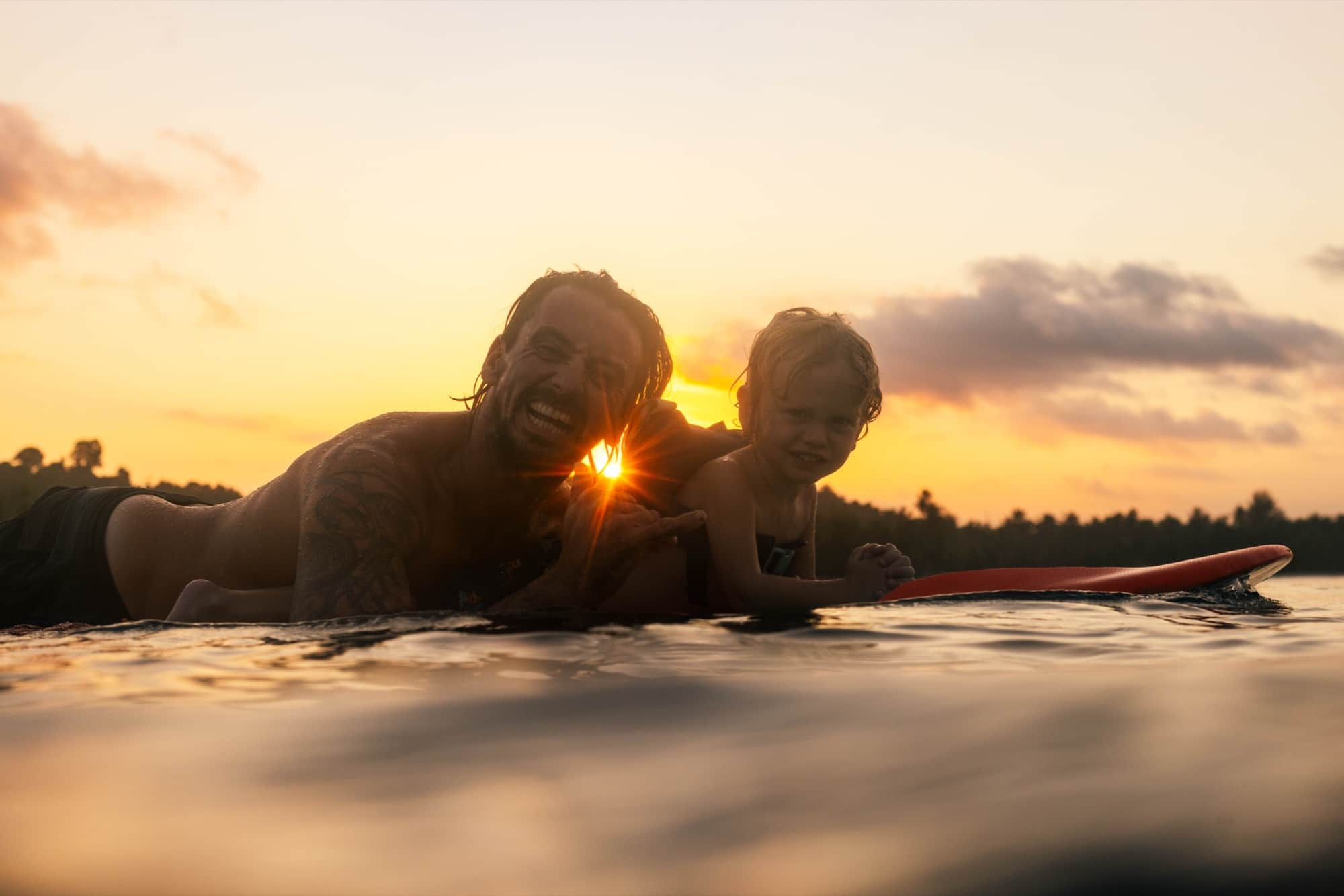 Two surfers paddling out at sunset